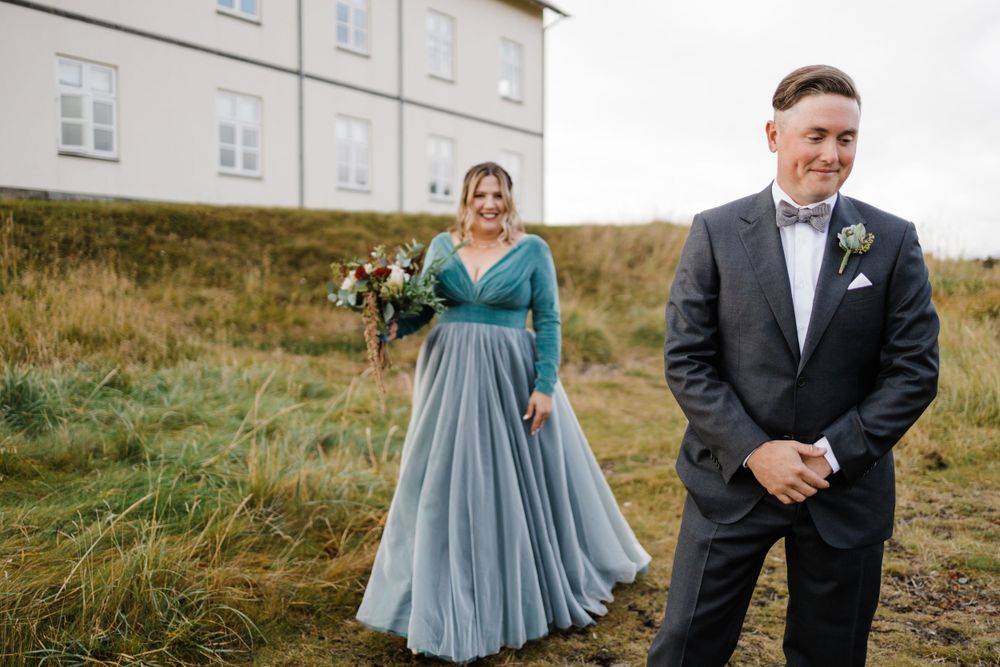 A couple shares a joyful first look moment outdoors with bride wearing a teal and grey flowing gown.