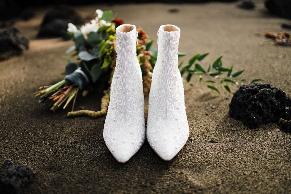 Pair of white bridal ankle boots with floral arrangements on textured background.