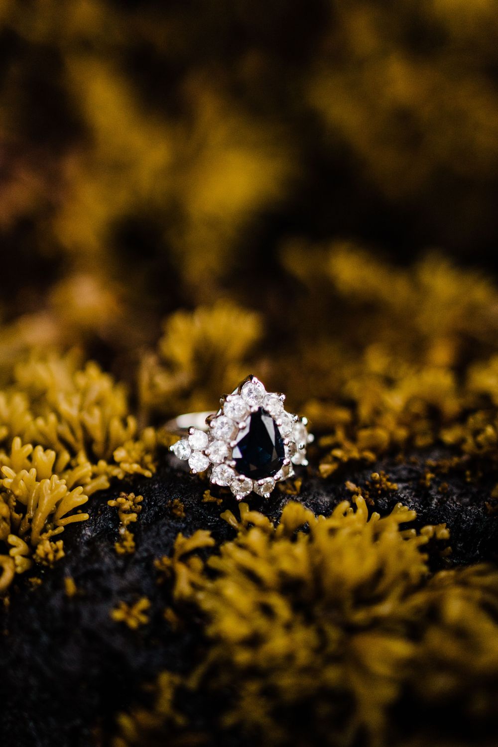 Elegant engagement ring with black center stone and diamond halo on textured yellow surface.