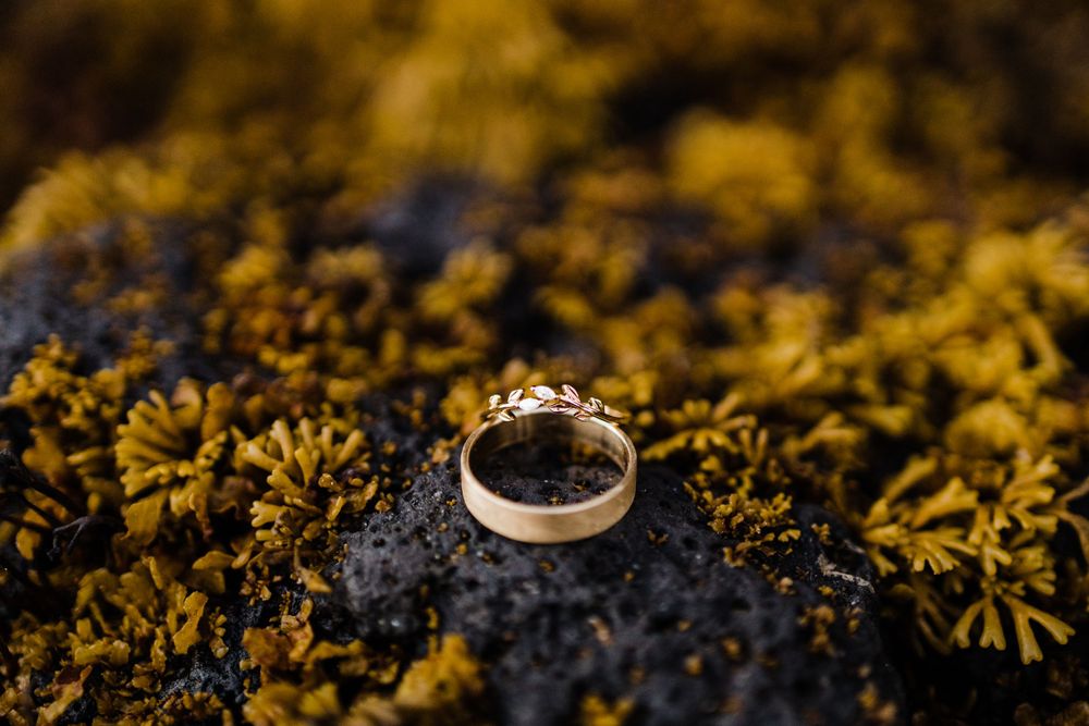 Golden wedding band photographed on black rock with yellow moss.