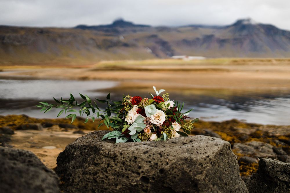 Wedding bouquet with white and pink flowers placed on rock with dramatic landscape background.