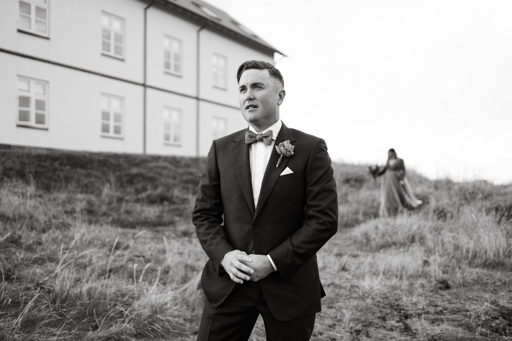 Formal portrait of groom in black tuxedo and bowtie against countryside backdrop.
