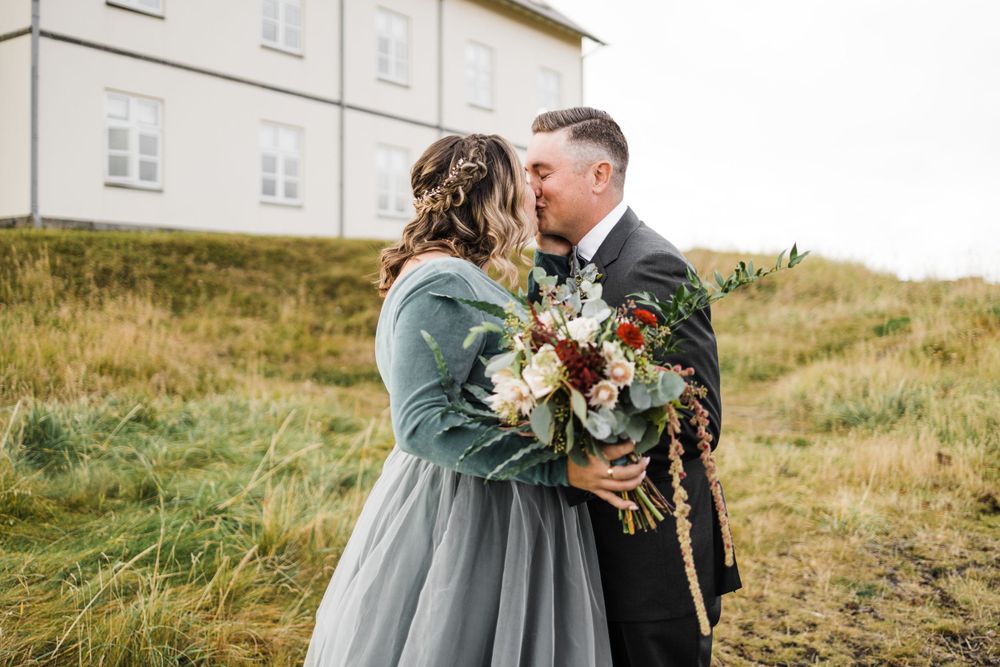 Wedding couple embracing outdoors in gray dress and black suit with autumn bouquet.