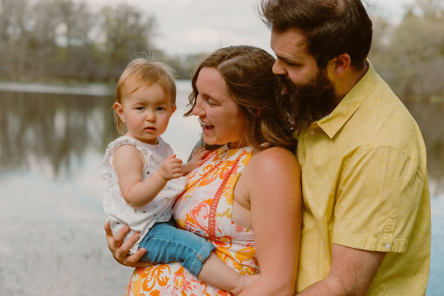 A happy young family shares a tender moment together by a serene lake on an overcast day.
