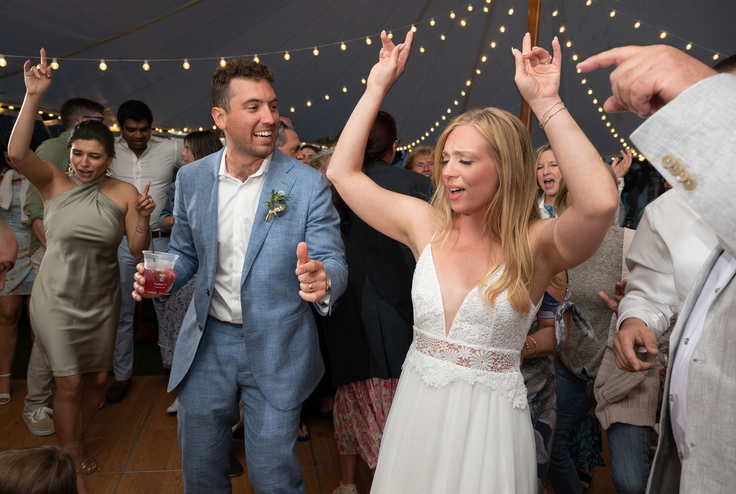 Wedding reception dance party with string lights and celebrating guests.