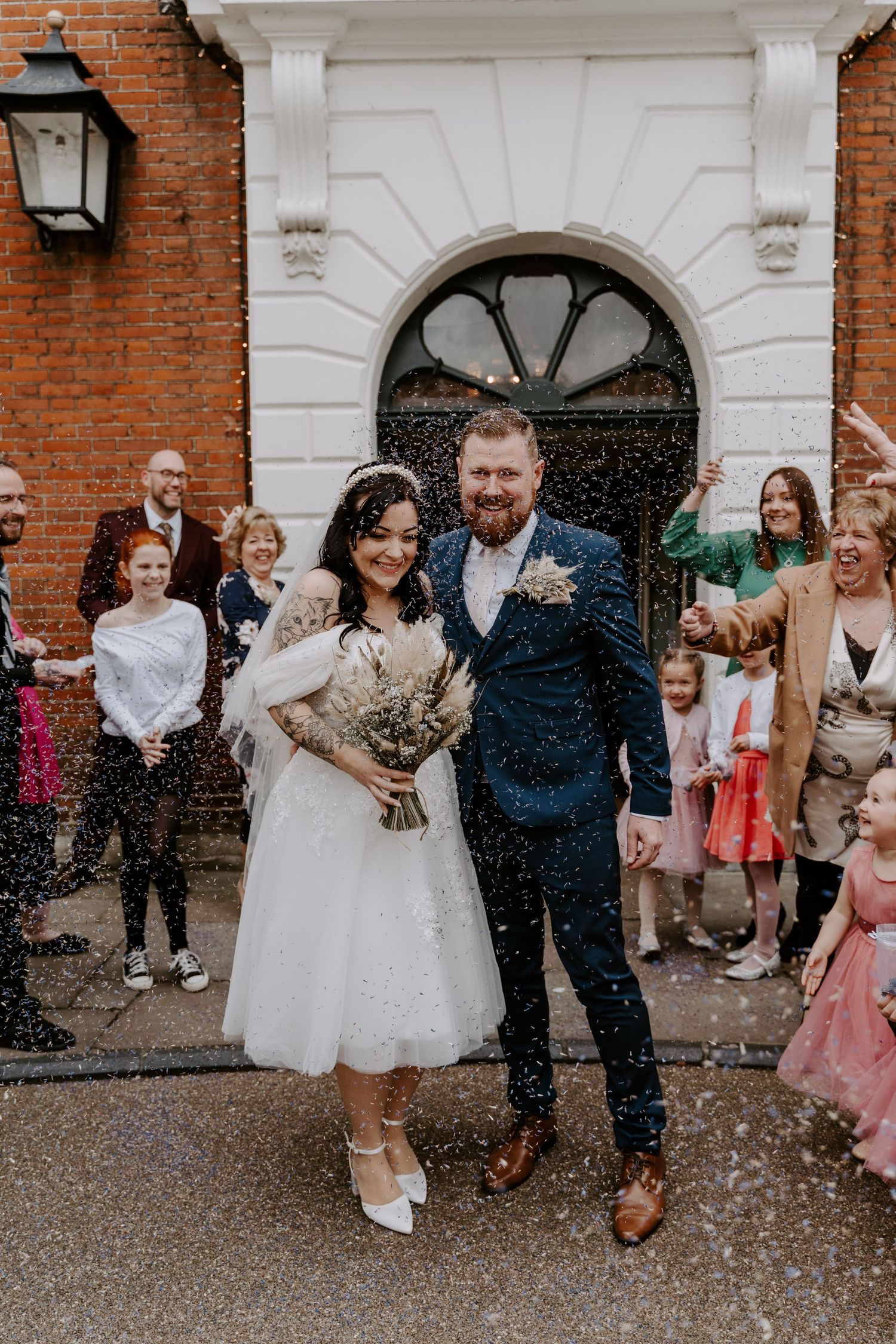 bride and groom laughing as guests throw purple confetti over them.