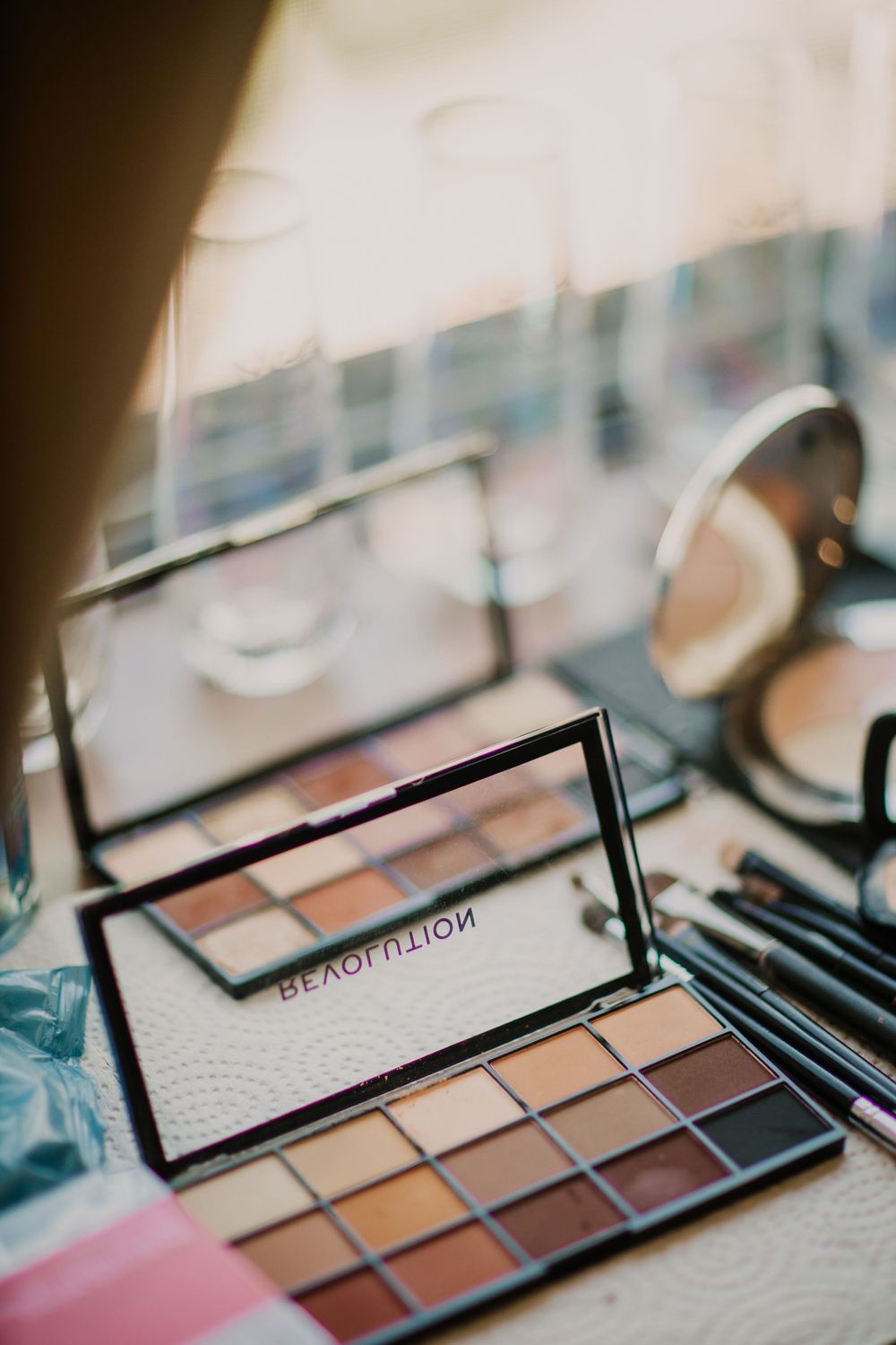 Makeup palette with neutral eyeshadow shades and mirror on vanity.