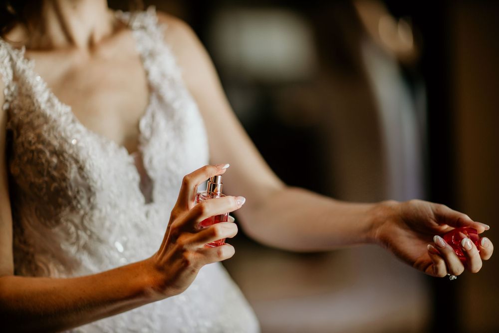 Hands applying perfume while wearing delicate lace wedding dress.