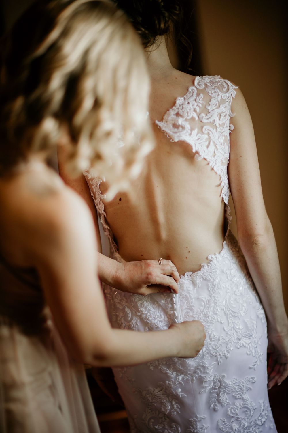 Intricate lace detailing on back of wedding dress being adjusted.