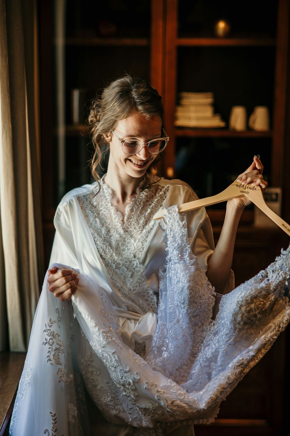 A bride in a white robe admires her wedding dress while getting ready.