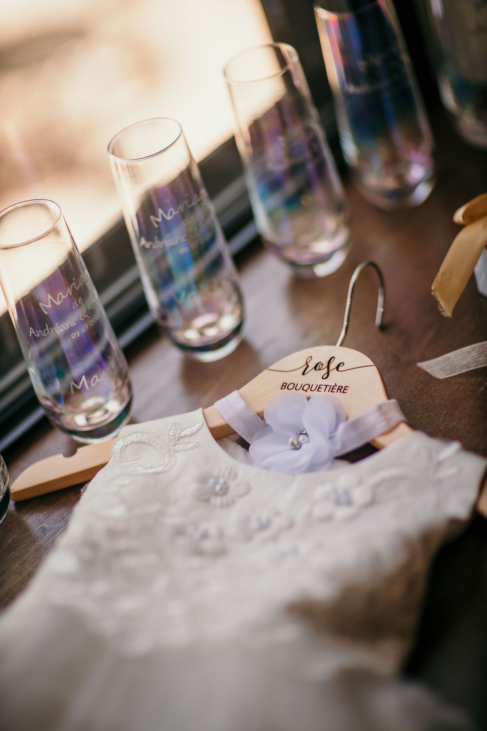 Iridescent champagne glasses and a white dress hanger arranged on a dark surface.