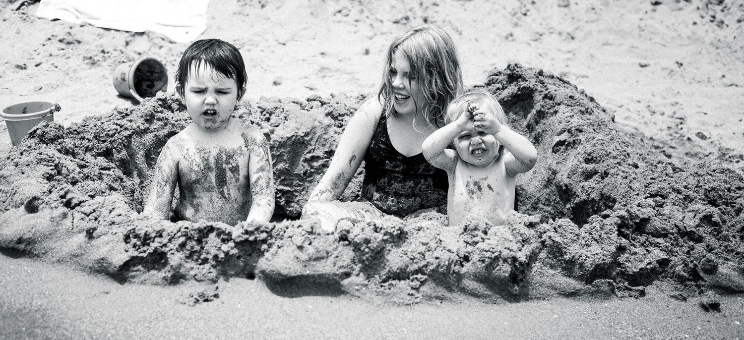 Three children getting dirty playing with the wet sand on the beach at family photo session