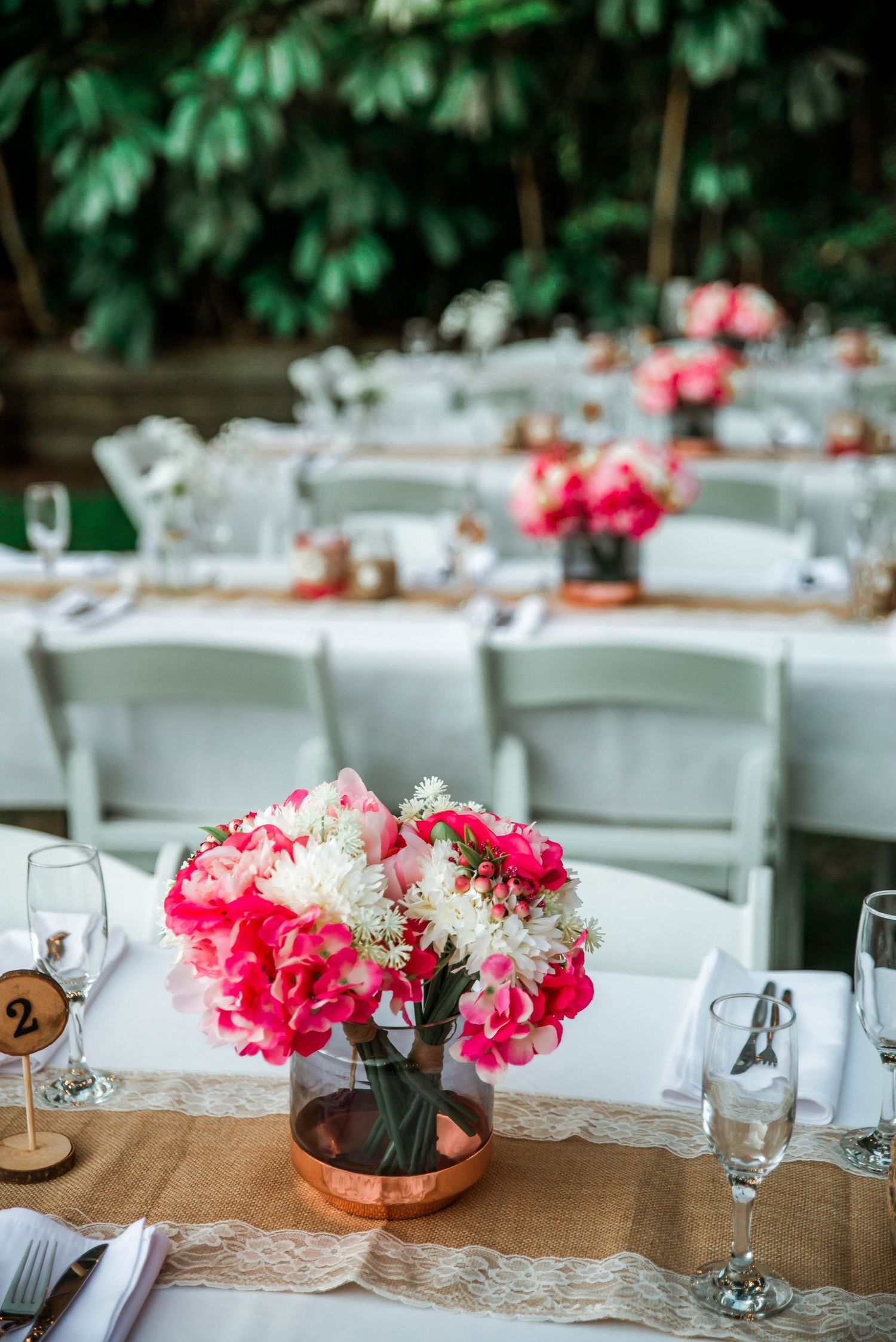 Elegant table setting with pink floral centerpieces and white folding chairs.