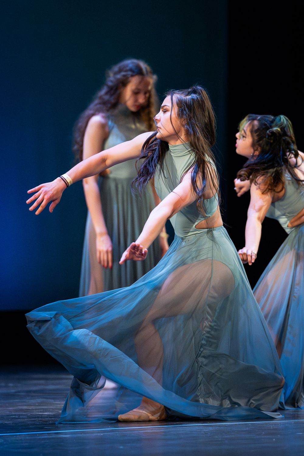 Dance ensemble performs contemporary routine in matching gray dresses on dark stage.