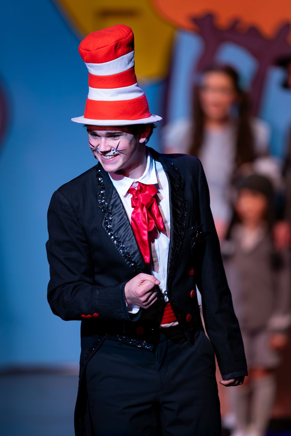 Performer in Cat in the Hat costume with striped hat and black suit jacket on stage.