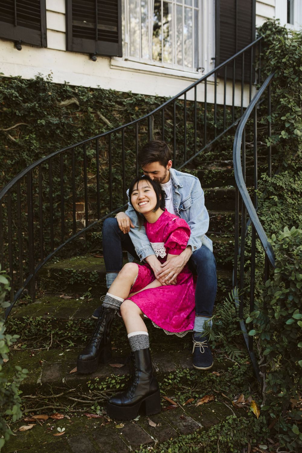 Playful engagement session in garden setting with pink dress and casual attire.