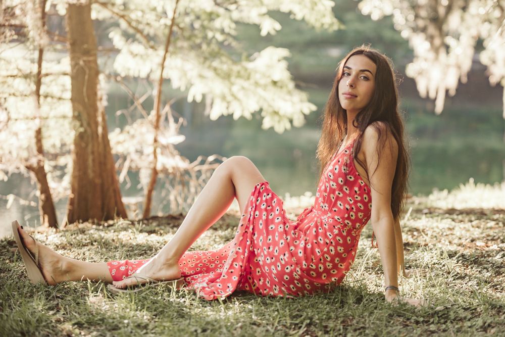 A person in a red floral dress poses gracefully on grass during a golden hour photoshoot.