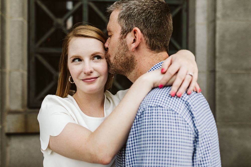 Couple embracing against stone building wall in casual attire.