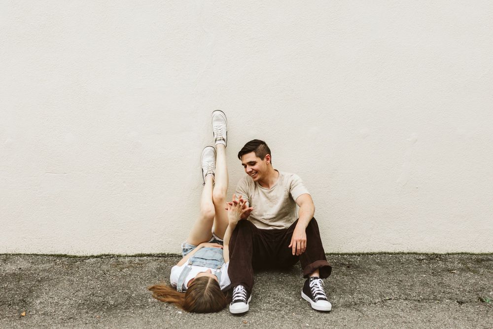Two people sitting casually on a concrete surface while playing acoustic guitars.