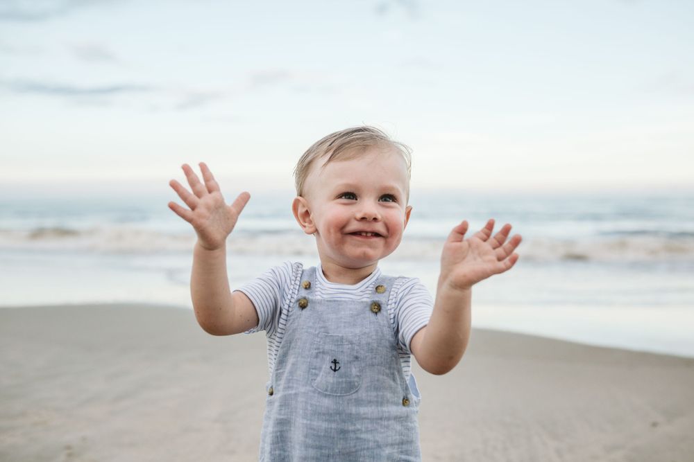 Joyful child in grey outfit playing on sunny beach with arms raised.