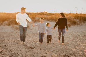 Family holding hands while running together on sandy beach at sunset.