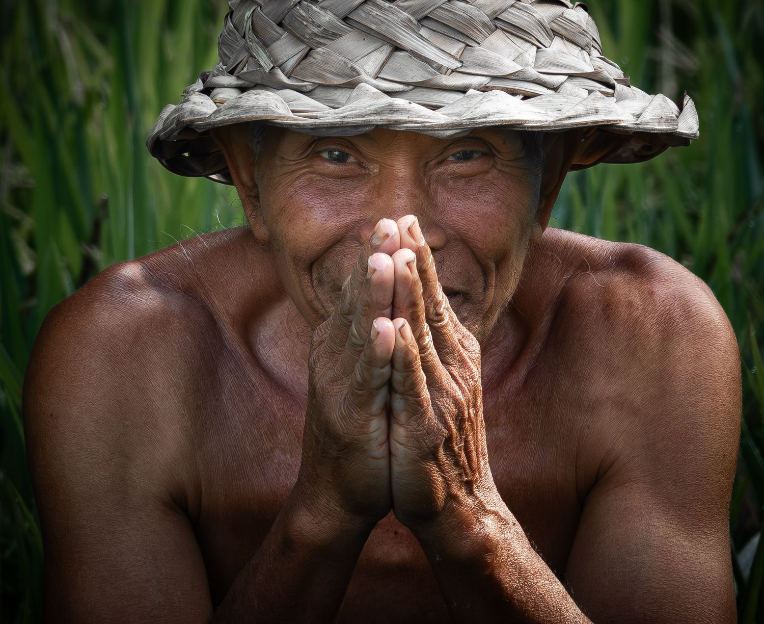 Traditional farmer in woven hat making prayer gesture in rice field.