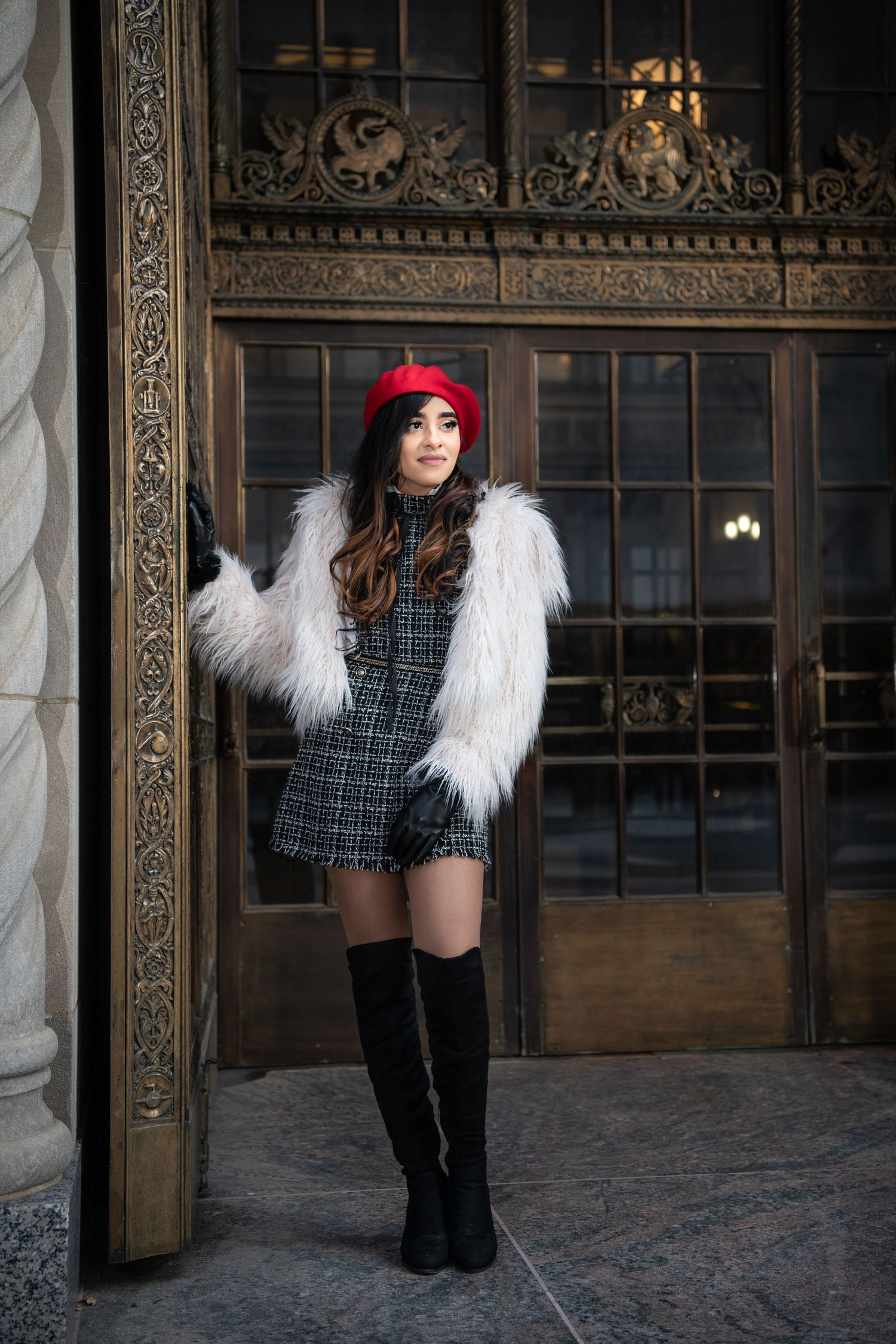 Stylish winter fashion with white fur coat and red beret against ornate architectural details.