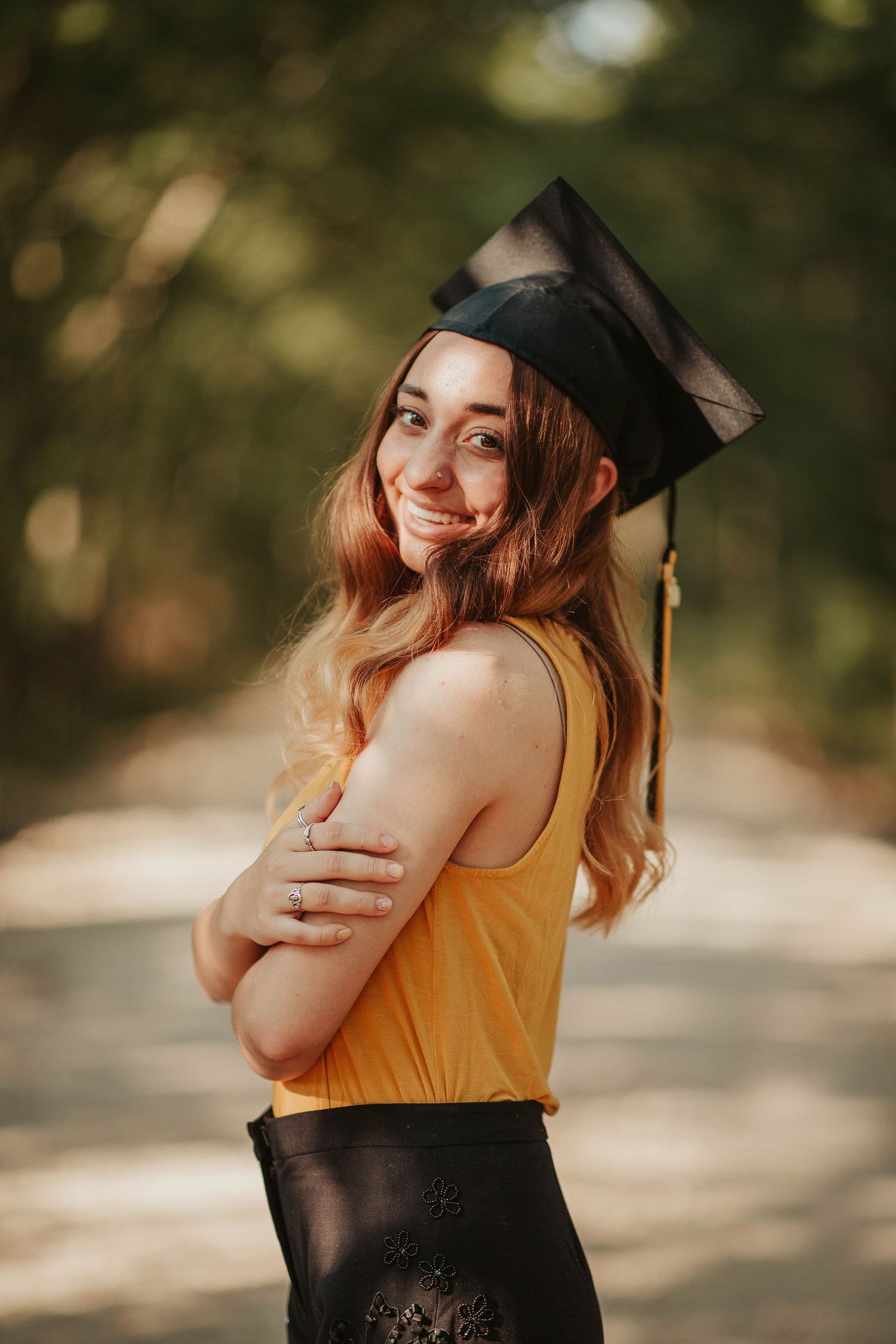 Graduate in a yellow top and graduation cap posing with a warm smile outdoors.
