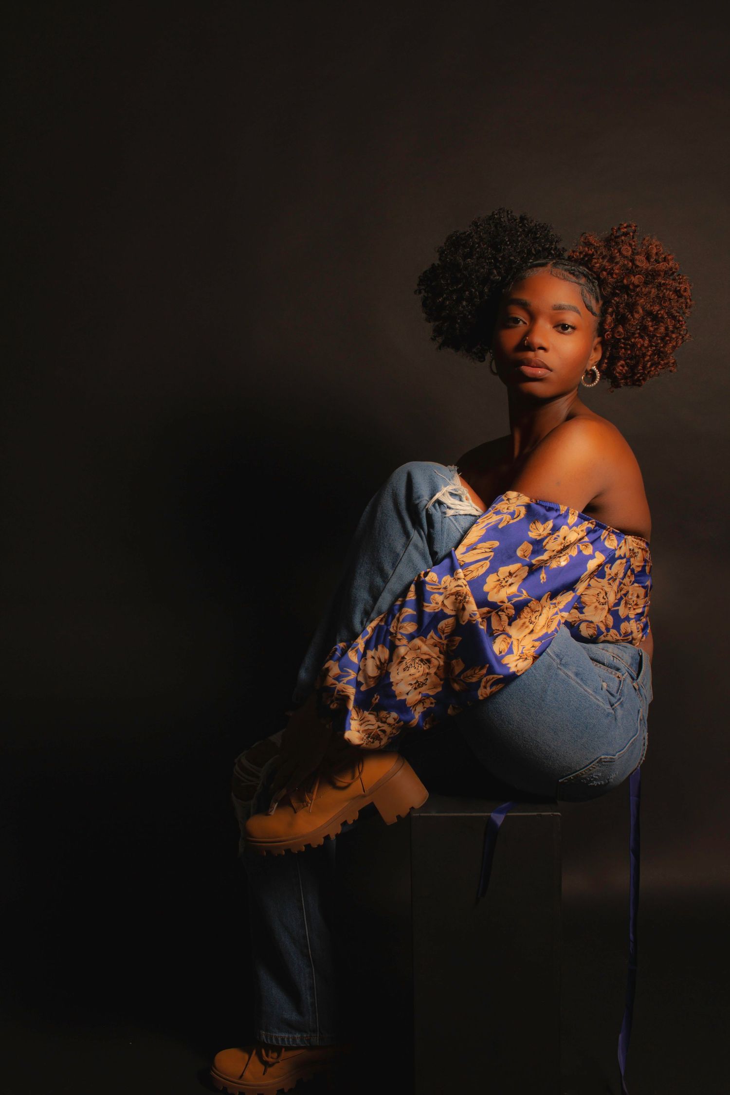 Artistic portrait of person in denim and floral top against dark background.