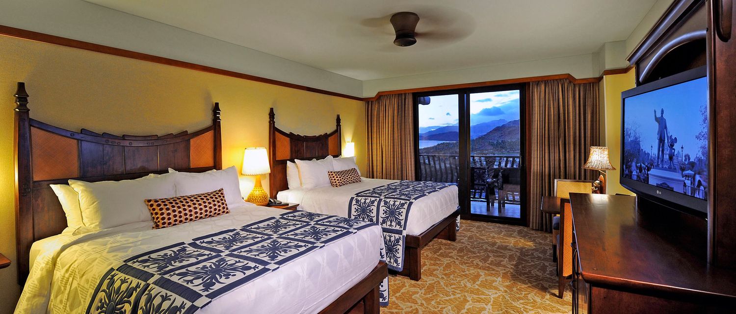 Elegant Hawaiian resort bedroom with two queen beds, tropical decor, and a balcony with mountain views.