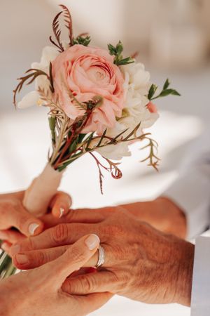 Delicate pink and white floral bouquet with intertwined hands showing wedding bands.