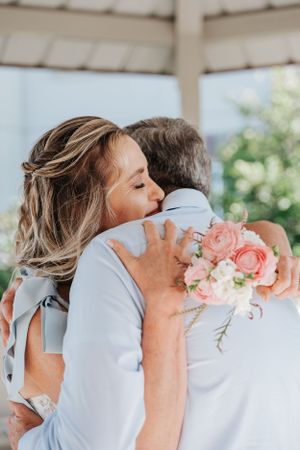 Tender wedding moment captured outdoors with pink roses and natural sunlight.