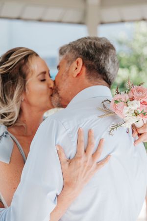 Romantic embrace with pink floral bouquet during outdoor wedding ceremony.