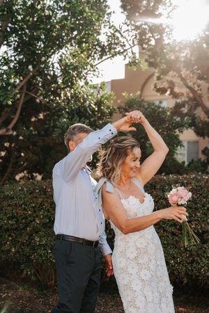 Couple dancing together in garden setting with pink bouquet at sunset.