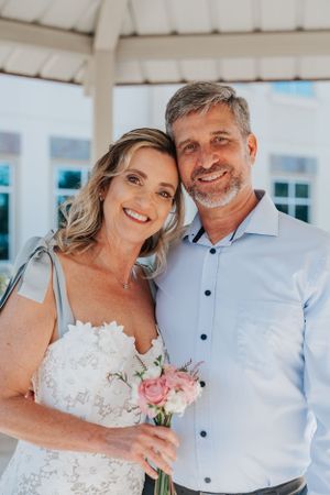 Happy wedding portrait under white gazebo with bride holding pink and white bouquet.