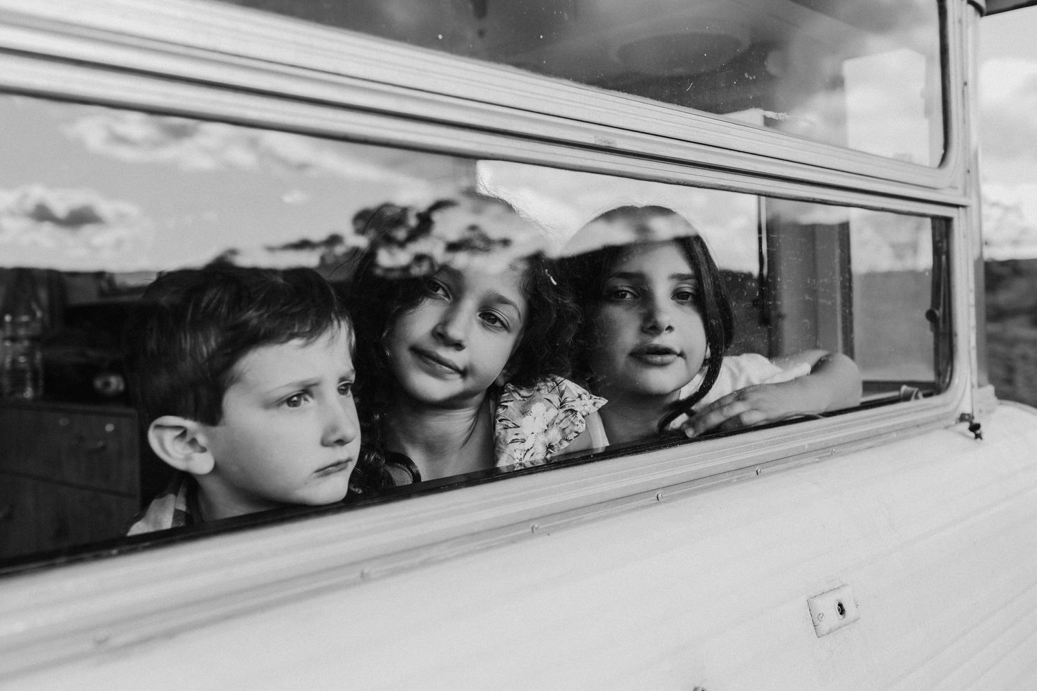 Three children peering through a bus window in a black and white photo.