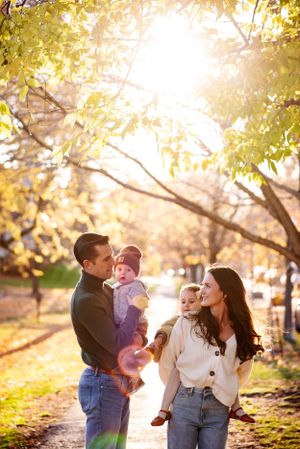 A young family, mom, dad and two children interacting in a park while the sun is setting