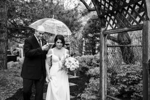 A father walking down his daughter, the bride, while holding an umbrella
