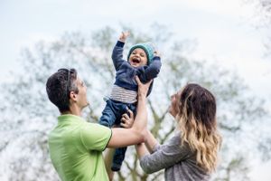 A mom and dad play throwing a young child in the air