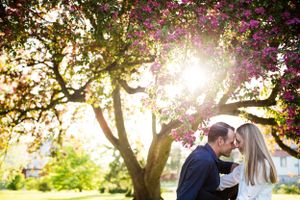 A young couple sitting on the ground forehead to forehead in front of a blooming tree
