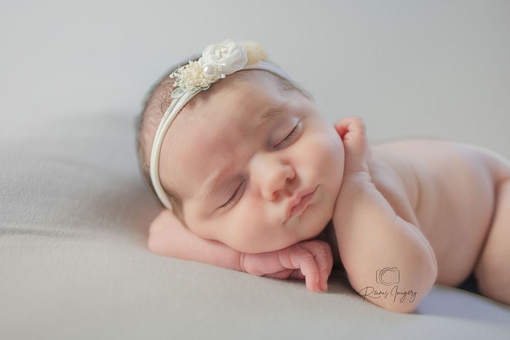 Peaceful sleeping newborn baby girl wearing delicate floral headband resting on soft gray blanket.