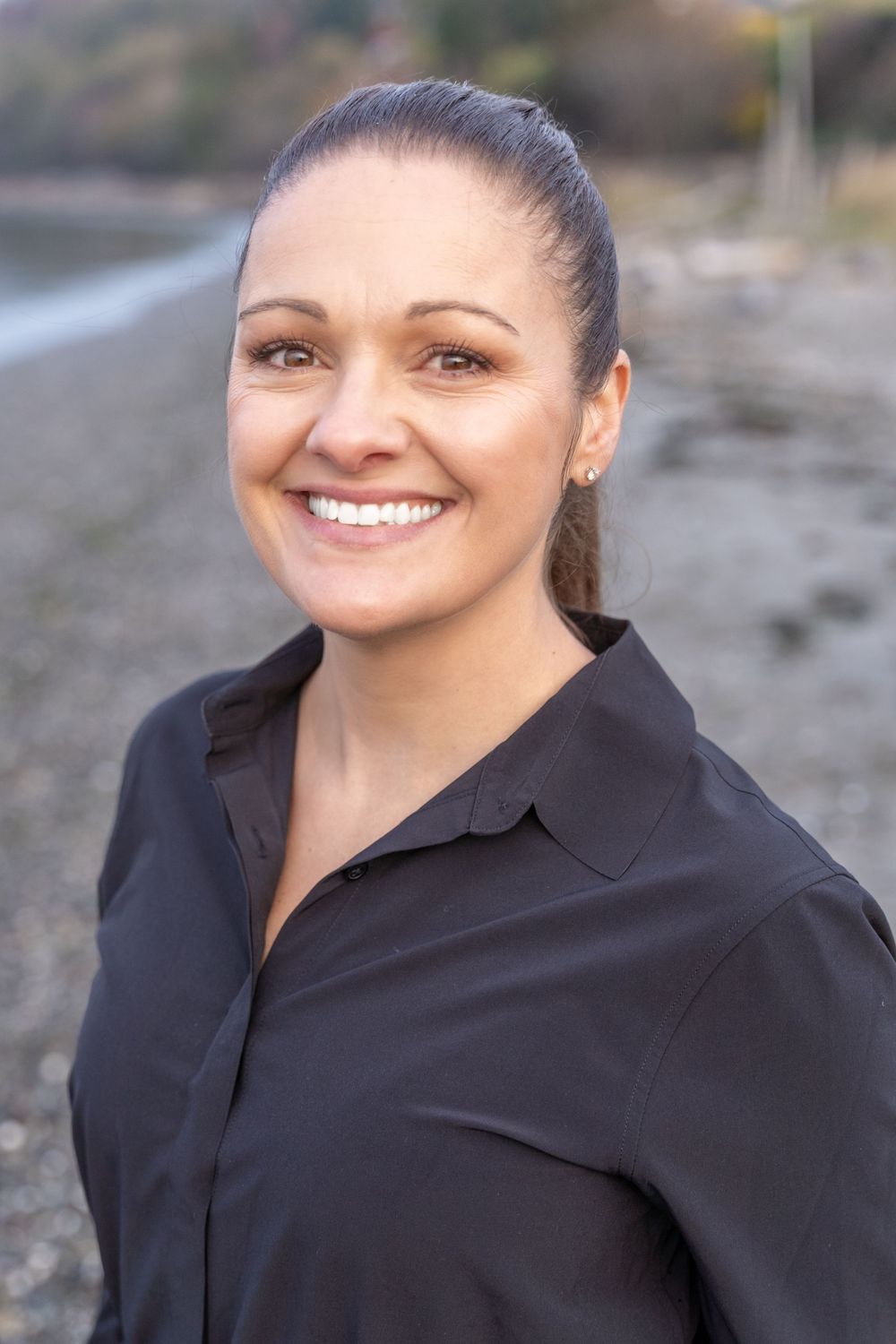 Professional headshot of person wearing black button-up against rocky beach background.