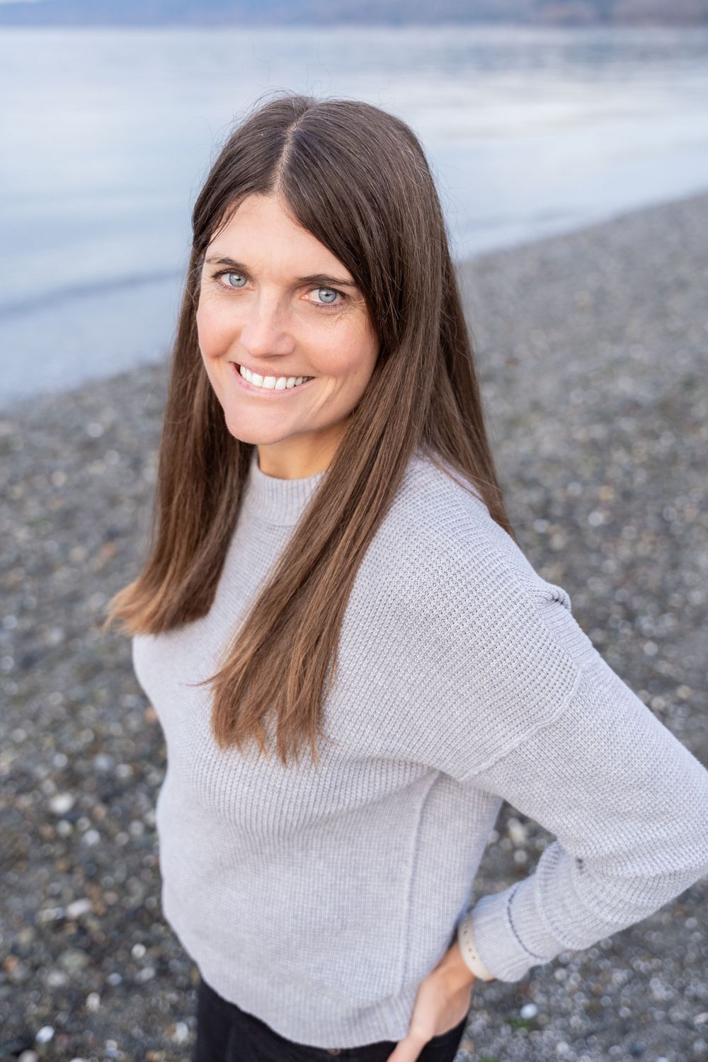 Portrait of person in light sweater smiling against beach landscape.