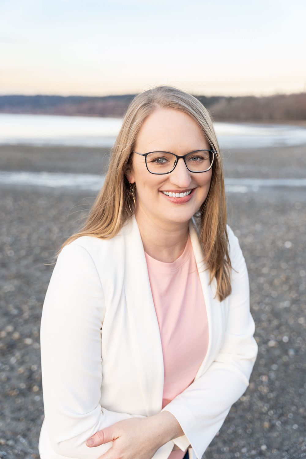Professional portrait on rocky beach wearing white blazer and pink top.
