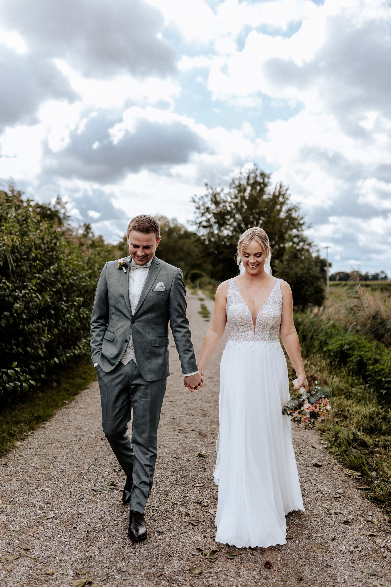 Elegant couple walking down country path under cloudy sky.