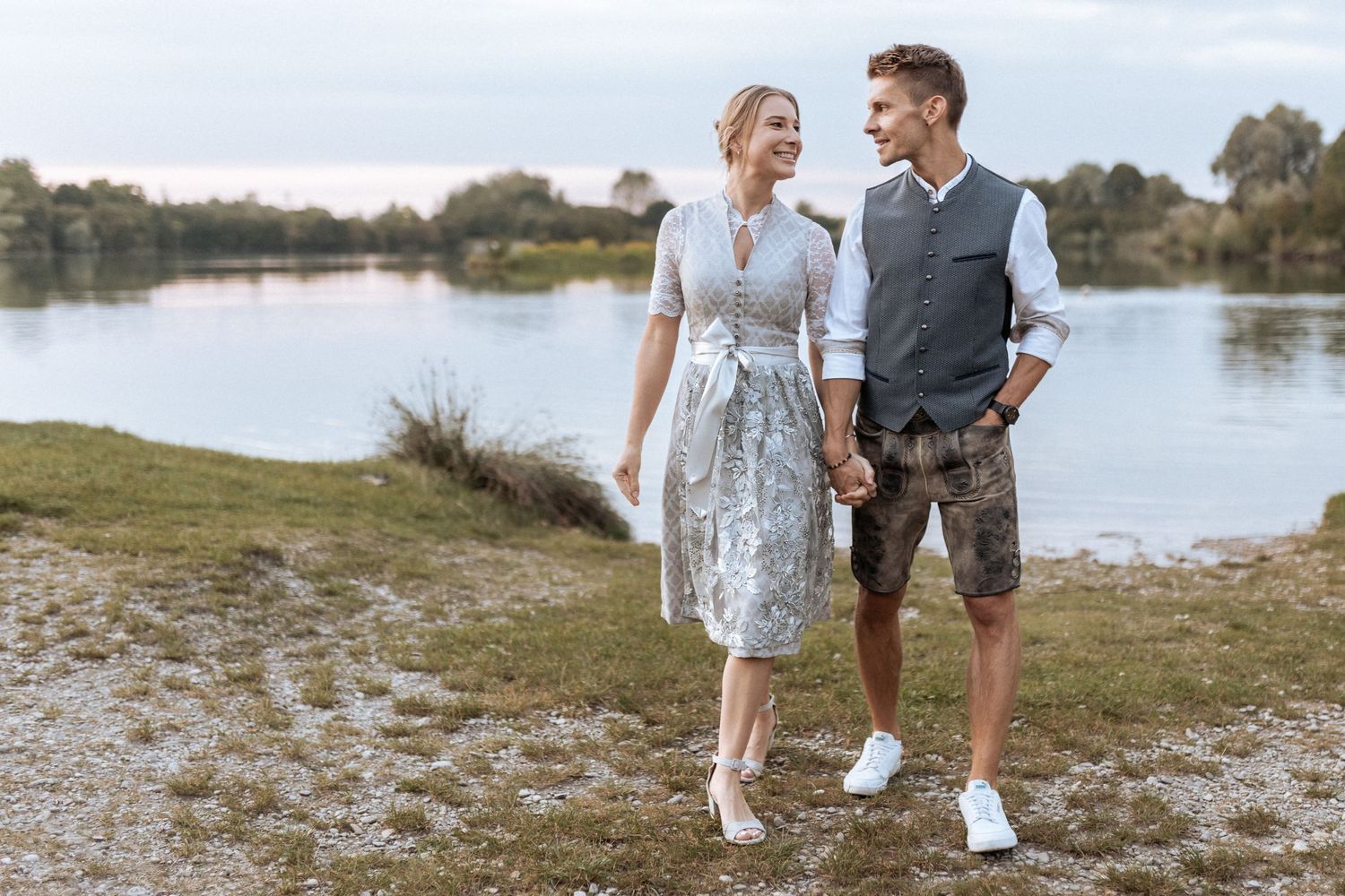 Couple in traditional Bavarian attire poses by lakeside with casual summer wedding style.