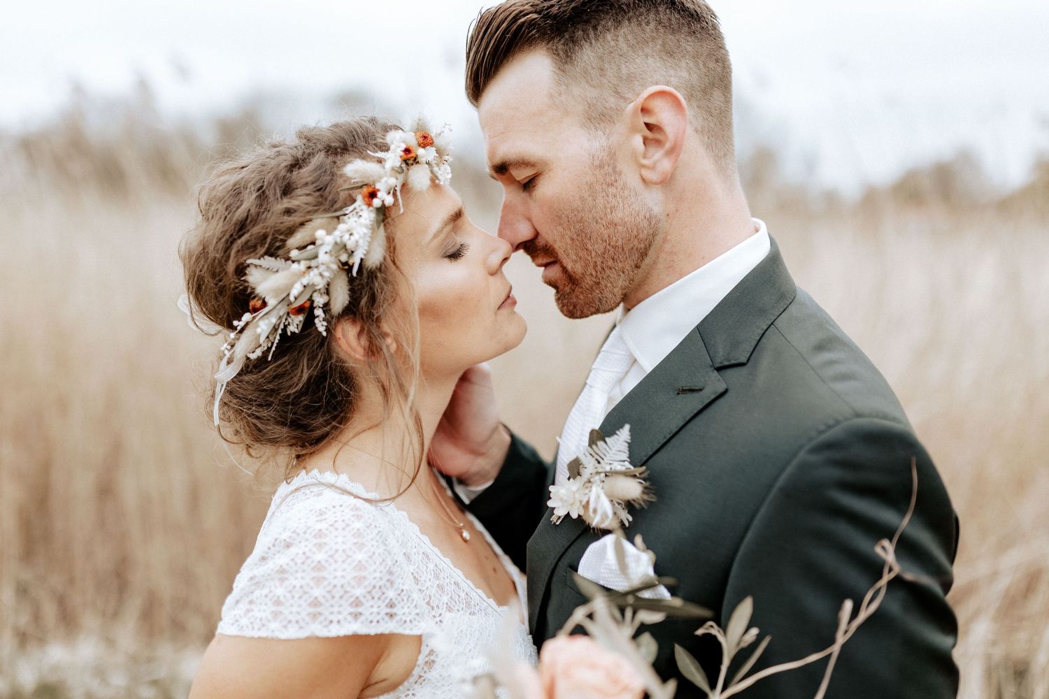 Intimate wedding portrait in tall grass with gentle romantic moment.
