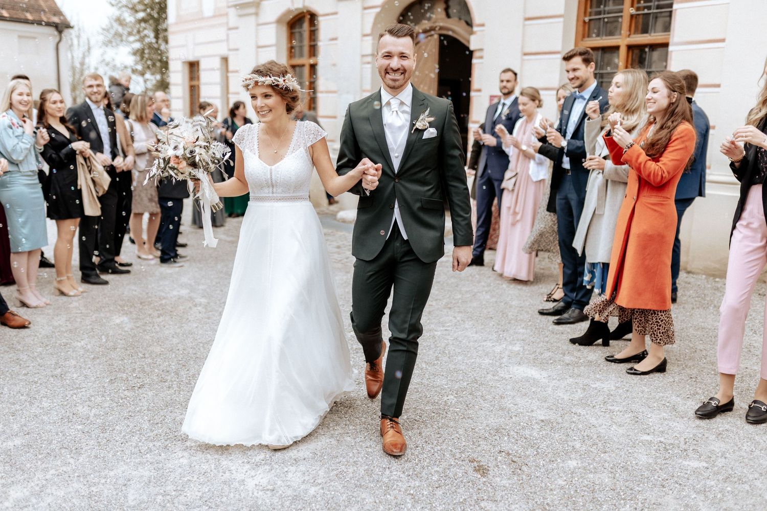 Newlyweds walking through crowd of wedding guests outside historic building.