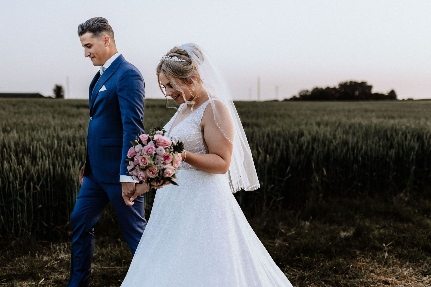Couple stands in golden wheat field during sunset wedding portrait session.