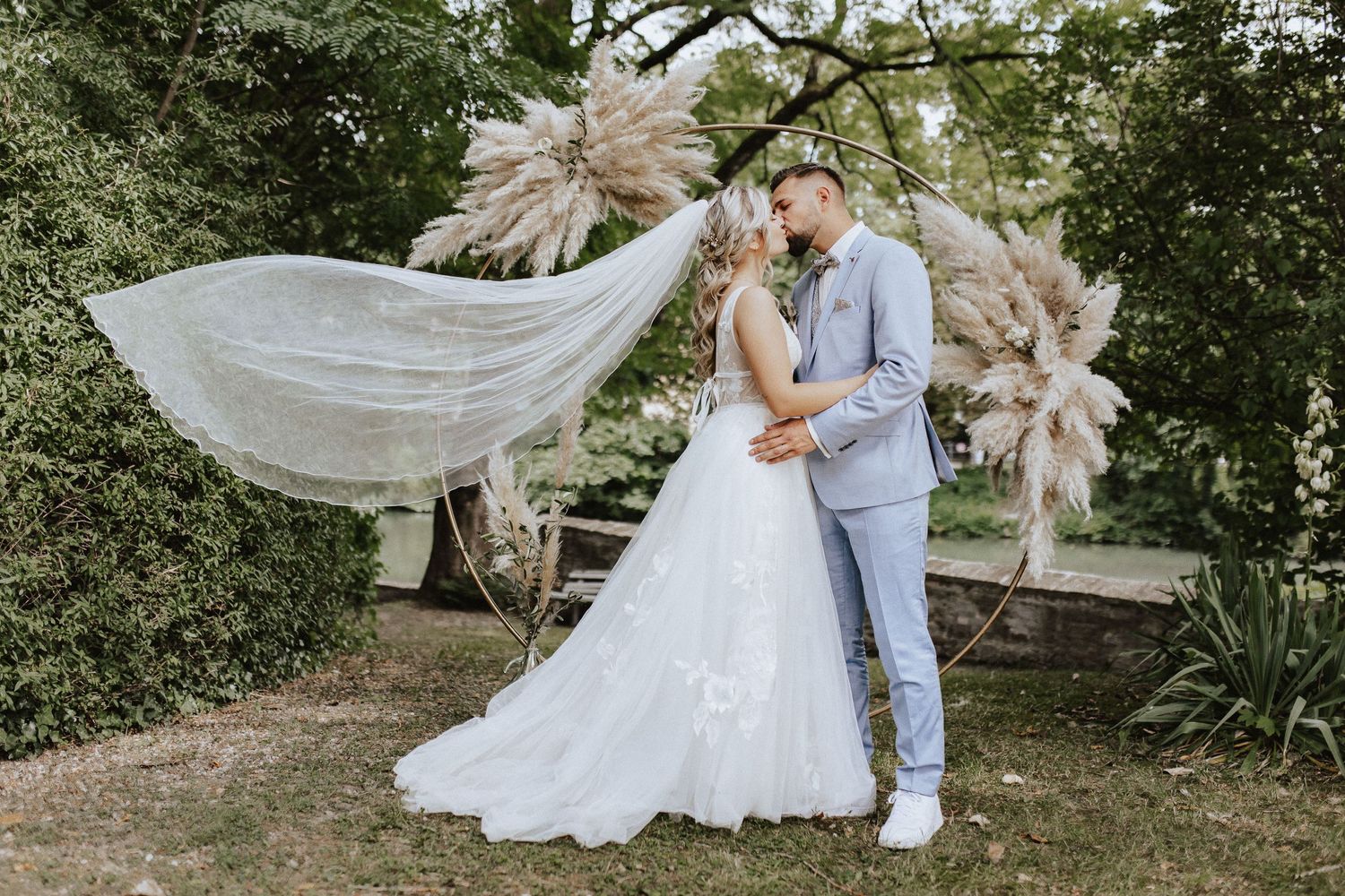 Couple poses under bohemian pampas grass arch in garden wedding setting.